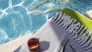 Vista de la piscina con un vaso de bebida, una toalla y los pies de una persona en el agua.