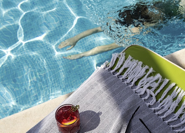 Vista de la piscina con un vaso de bebida, una toalla y los pies de una persona en el agua.