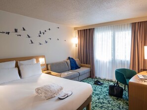 A hotel room with a bed, a sofa, a desk, and a chair. - Demeures de campagne Orleans Chemin de Sologne – Novotel (Orléans)