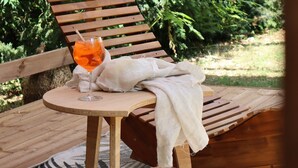 Une terrasse en bois avec une table ronde, un verre de boisson à l’orange et une nappe blanche.