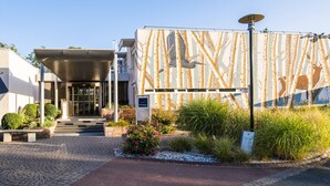 Una entrada de hotel moderna con un vestíbulo techado, un mural grande con animales y una antena parabólica.