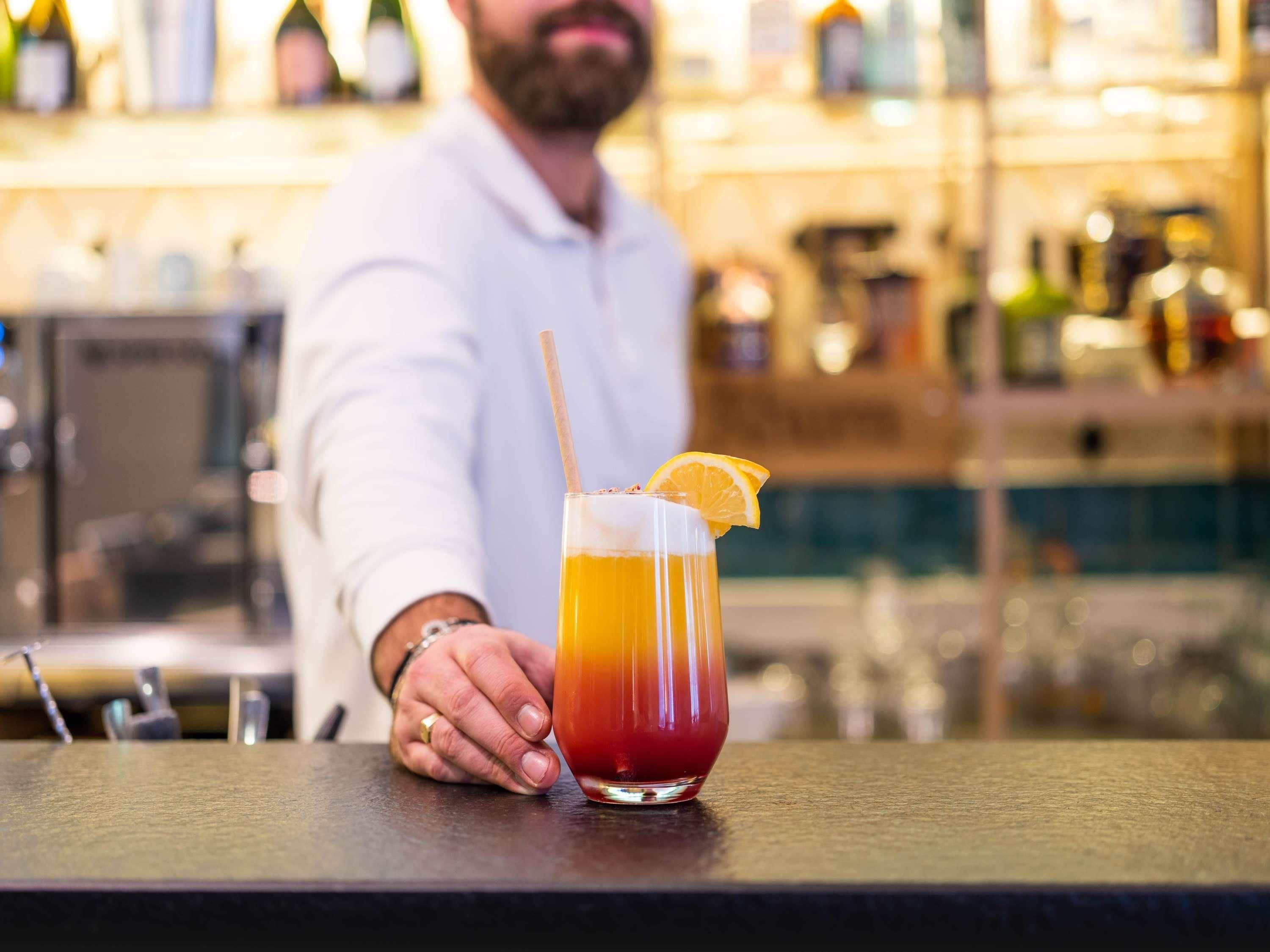 A bartender at a bar with a drink in a glass.