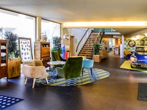 A spacious lobby with a staircase, modern furniture, and a vintage car display. - Demeures de campagne Orleans Chemin de Sologne – Novotel (Orléans)