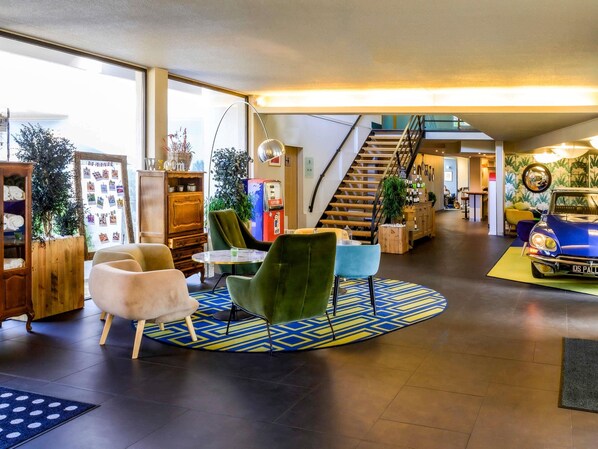 A spacious lobby with a staircase, modern furniture, and a vintage car display. - Demeures de campagne Orleans Chemin de Sologne – Novotel (Orléans)