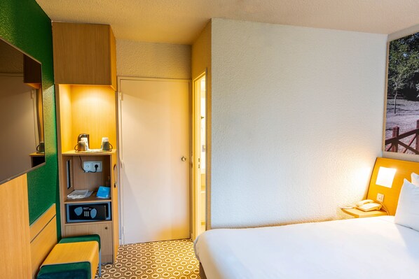 Habitación de hotel con cama, escritorio con computadora, microondas y un pequeño rincón de descanso.