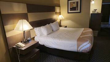 A hotel room with a bed, two bedside lamps, a nightstand with a telephone, and a framed picture on the wall.