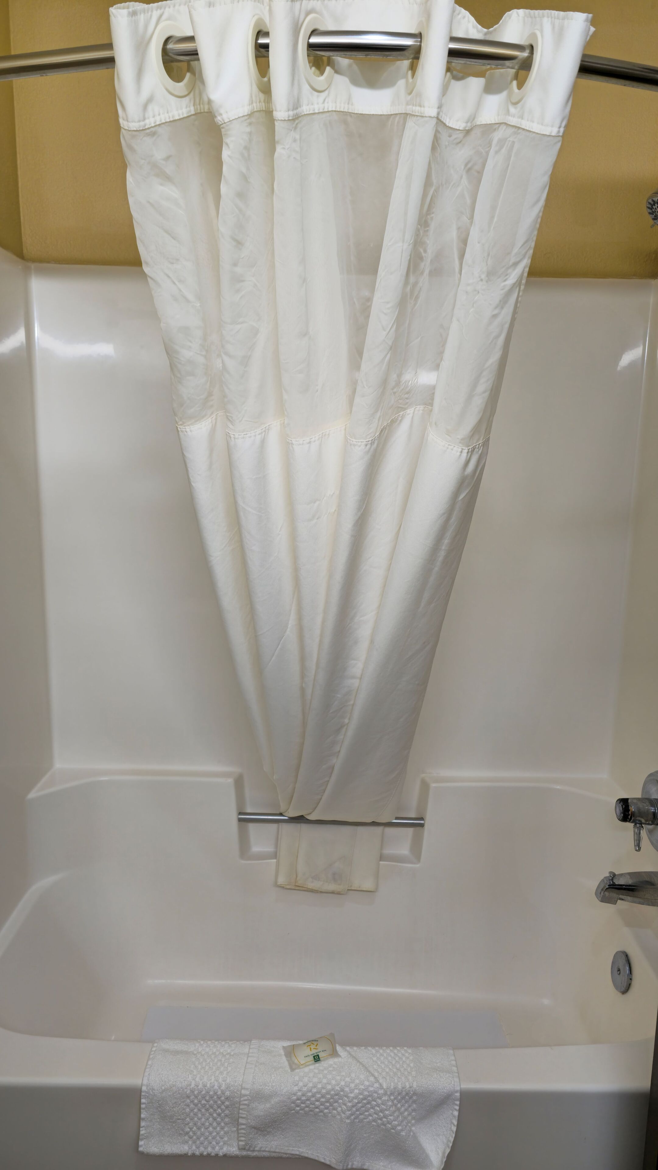 A bathtub with a white shower curtain and a white towel.