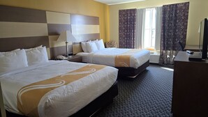 A hotel room with two beds, a desk, a lamp, and a TV.