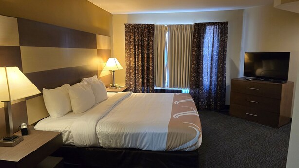 A hotel room with a bed, bedside lamps, a TV, a dresser, and curtains. - Haven Hotel (Shawano)