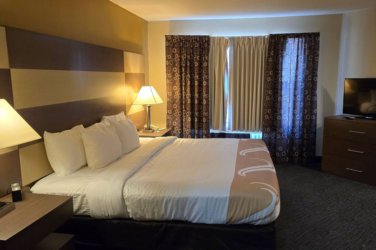 A hotel room with a bed, bedside lamps, a TV, a dresser, and curtains.