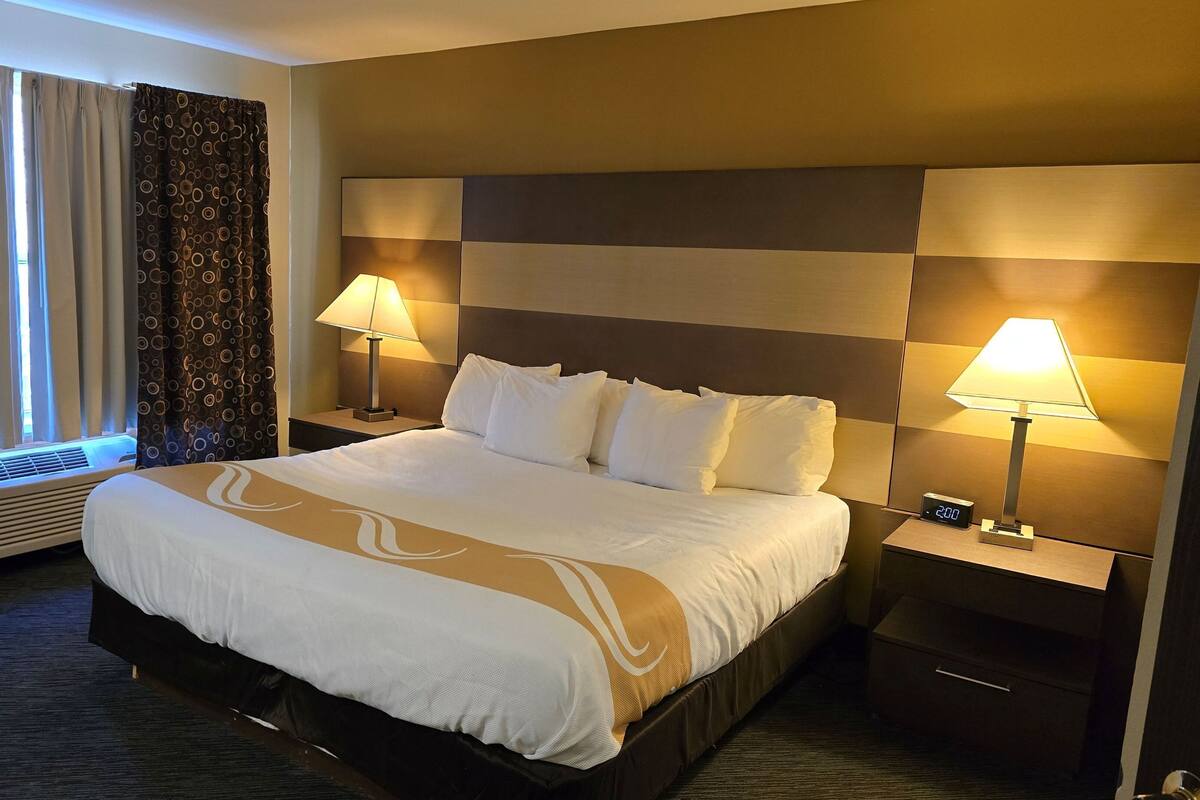 A hotel room with a large bed, two bedside lamps, a heater, and a window with curtains.