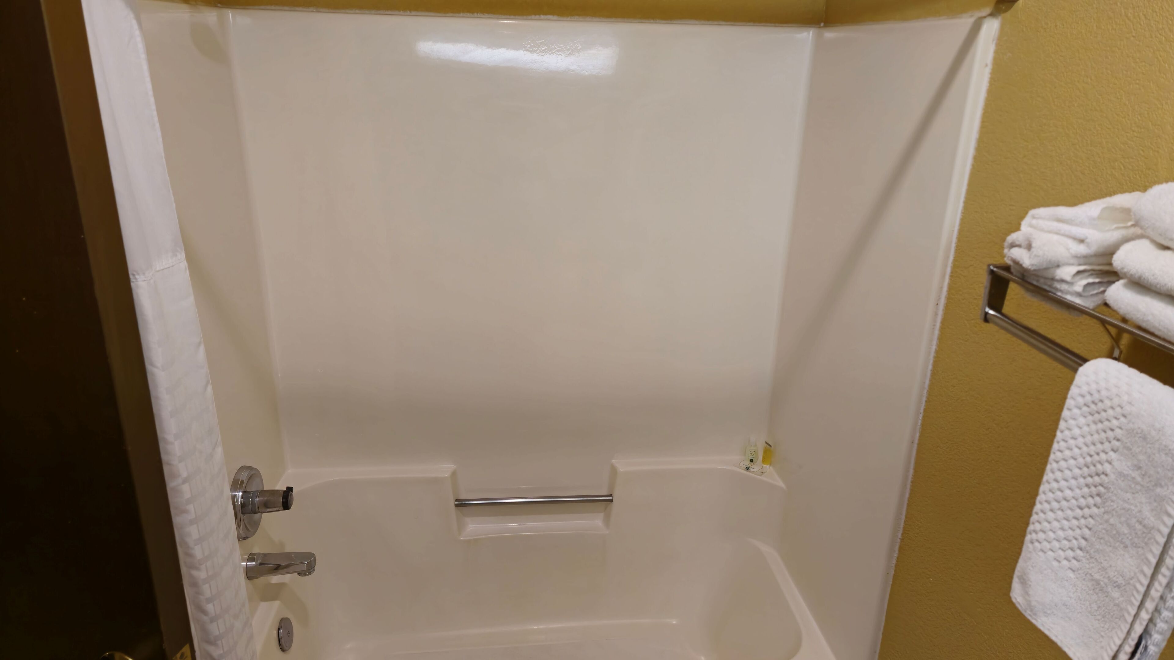 A bathroom with a white bathtub, a towel rack with folded towels, and a toilet.