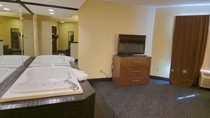 A hotel bathroom with two large tubs, a wooden cabinet with a television, and a carpeted floor. - Haven Hotel (Shawano)