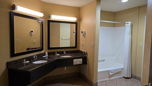 A bathroom with two sinks, a mirror, a hairdryer, and a shower.