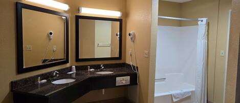 A bathroom with two sinks, a mirror, a hairdryer, and a shower.