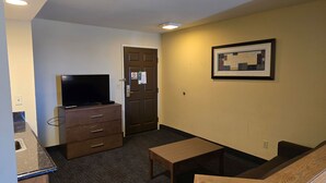 A hotel room with a flat-screen TV on a dresser, a small wooden table, and a framed abstract artwork on the wall. - Haven Hotel (Shawano)