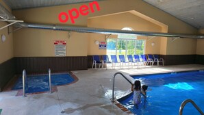 An indoor swimming pool area with a sign indicating 'open' and 'no lifeguard on duty'. - Haven Hotel (Shawano)