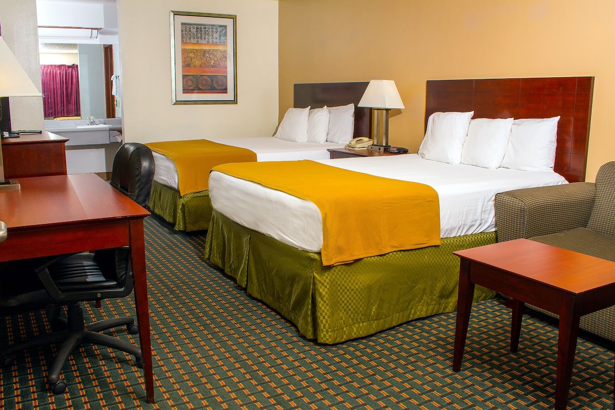 A hotel room with two beds, a desk, a chair, and a bathroom visible through an open door.