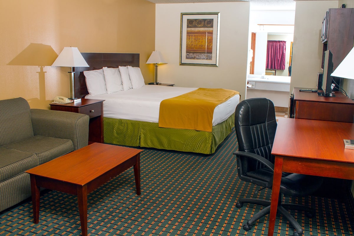 A hotel room with a bed, a desk, a chair, a sofa, and two lamps.