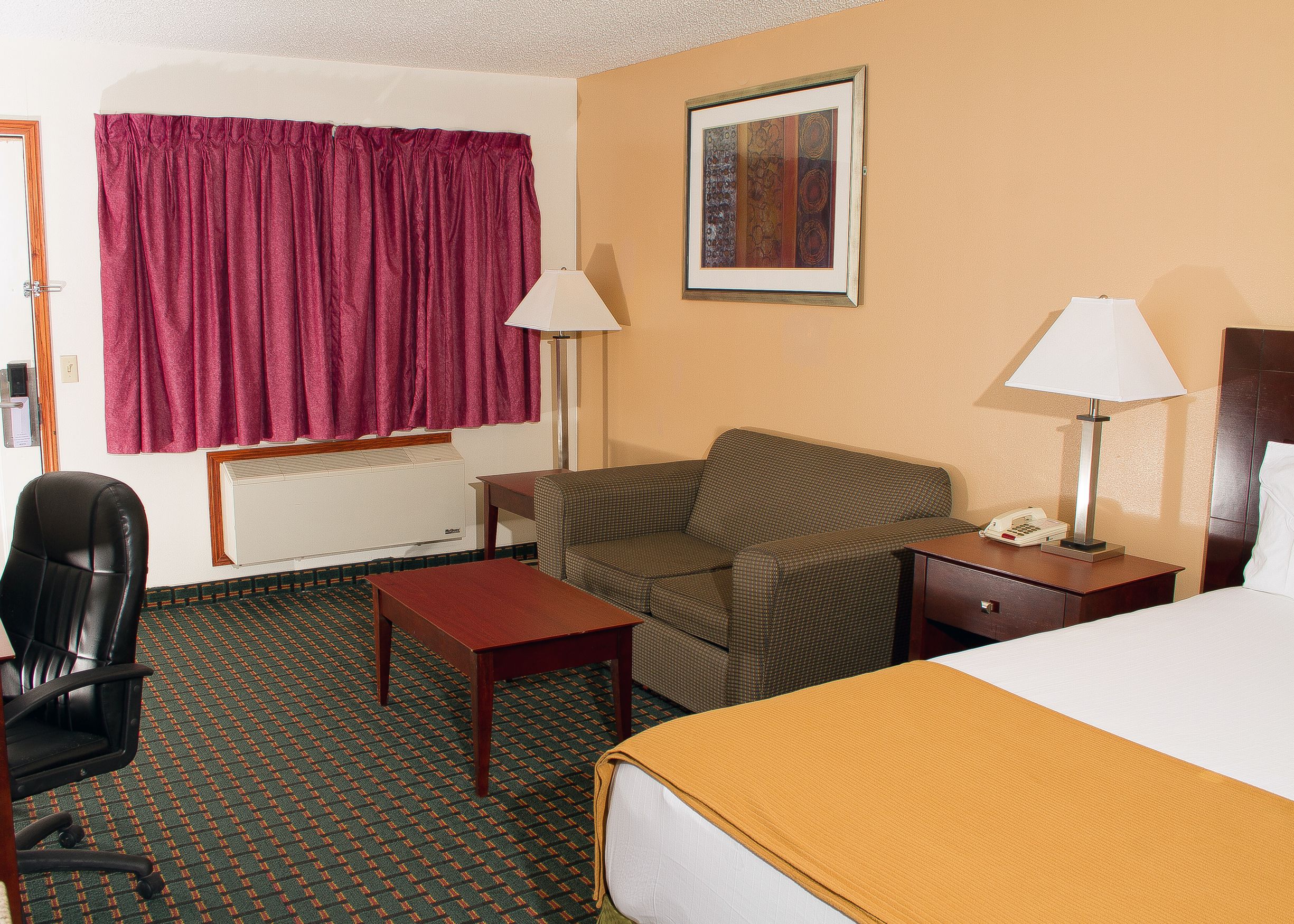 A hotel room with a bed, a chair, a desk, a lamp, and a painting on the wall.