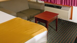 A hotel room with a bed, a sofa, a small table, a lamp, a window with curtains, and a radiator.