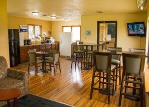 A hotel room with a kitchenette, dining area with multiple chairs, a sofa, and a television.