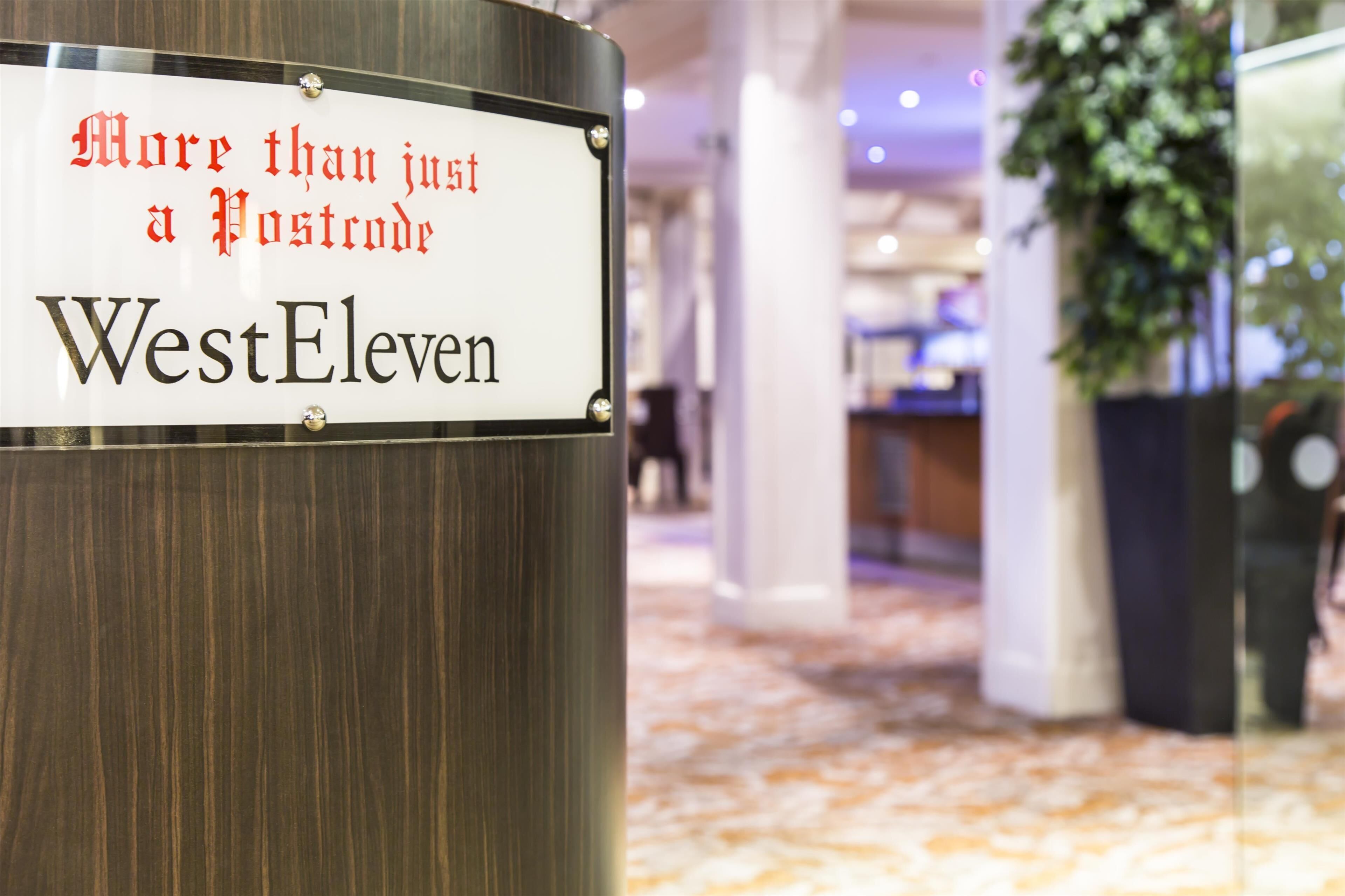 Ein Schild mit dem Text „More than just a Postcode WestEleven“ an einem Metallpfosten befestigt.