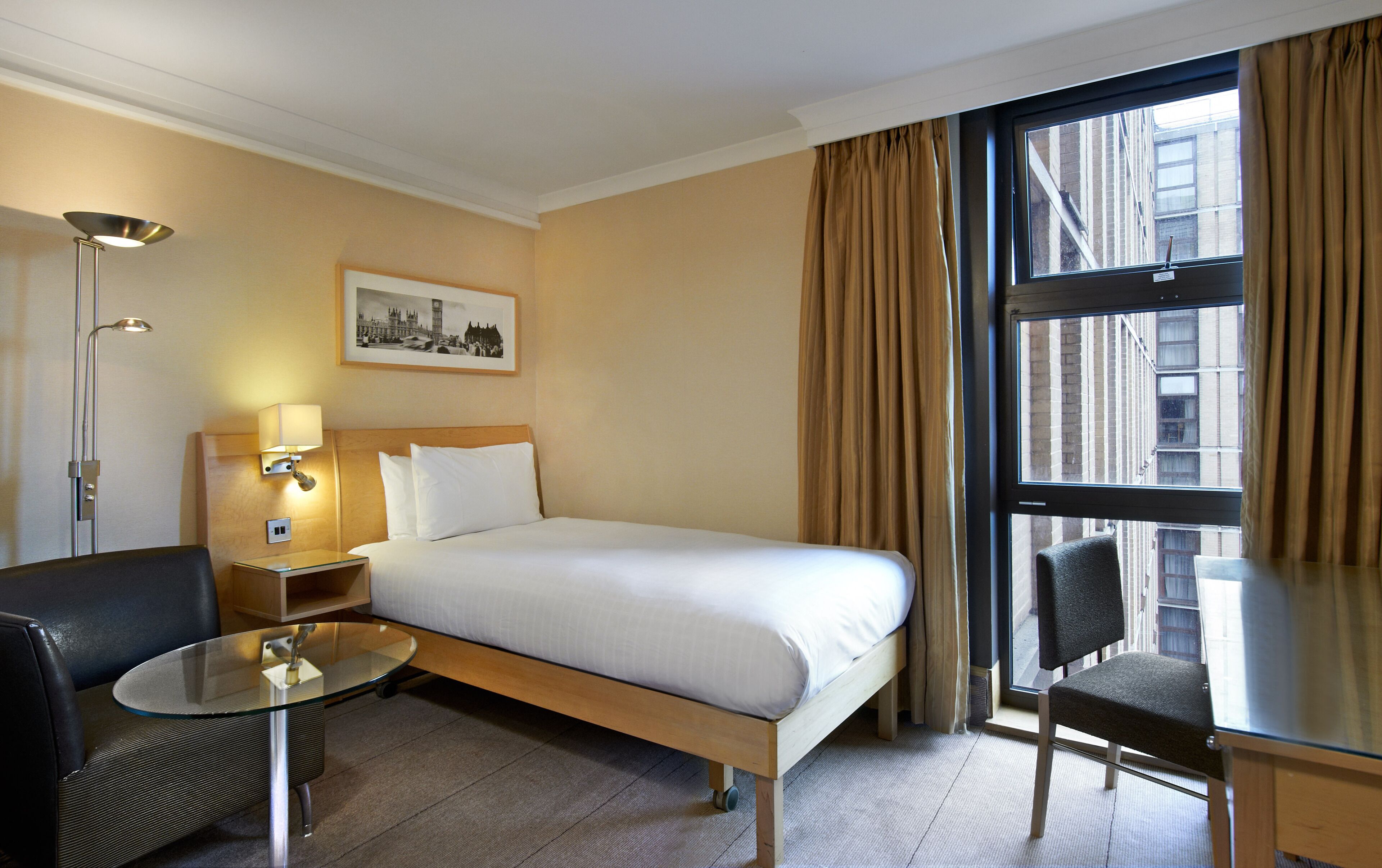 A hotel room with a bed, a desk, a chair, a lamp, and a window with curtains.