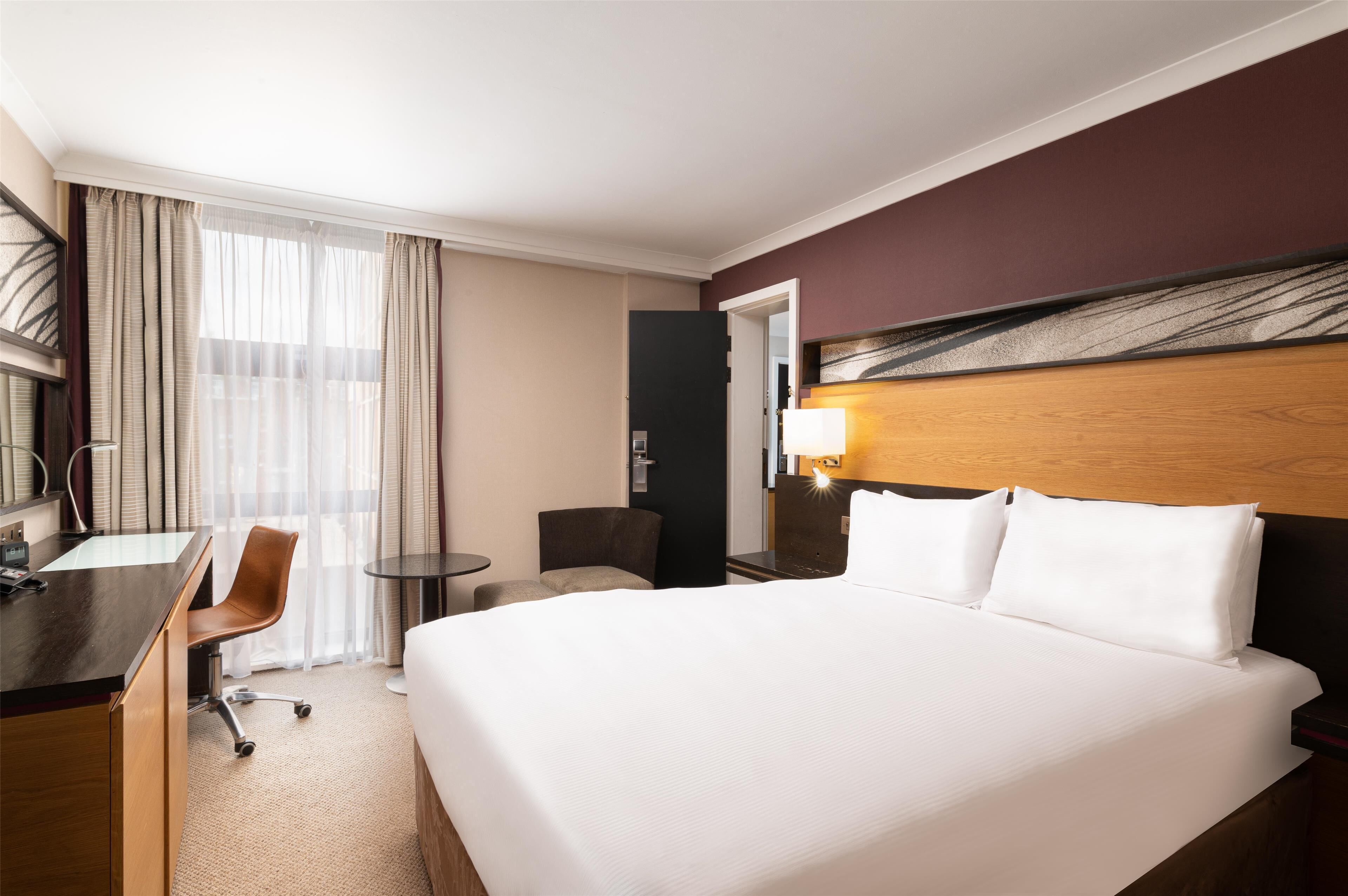 Ein Hotelzimmer mit einem großen Bett, einem Schreibtisch, einem Sessel, einem kleinen Tisch und einer Lampe.