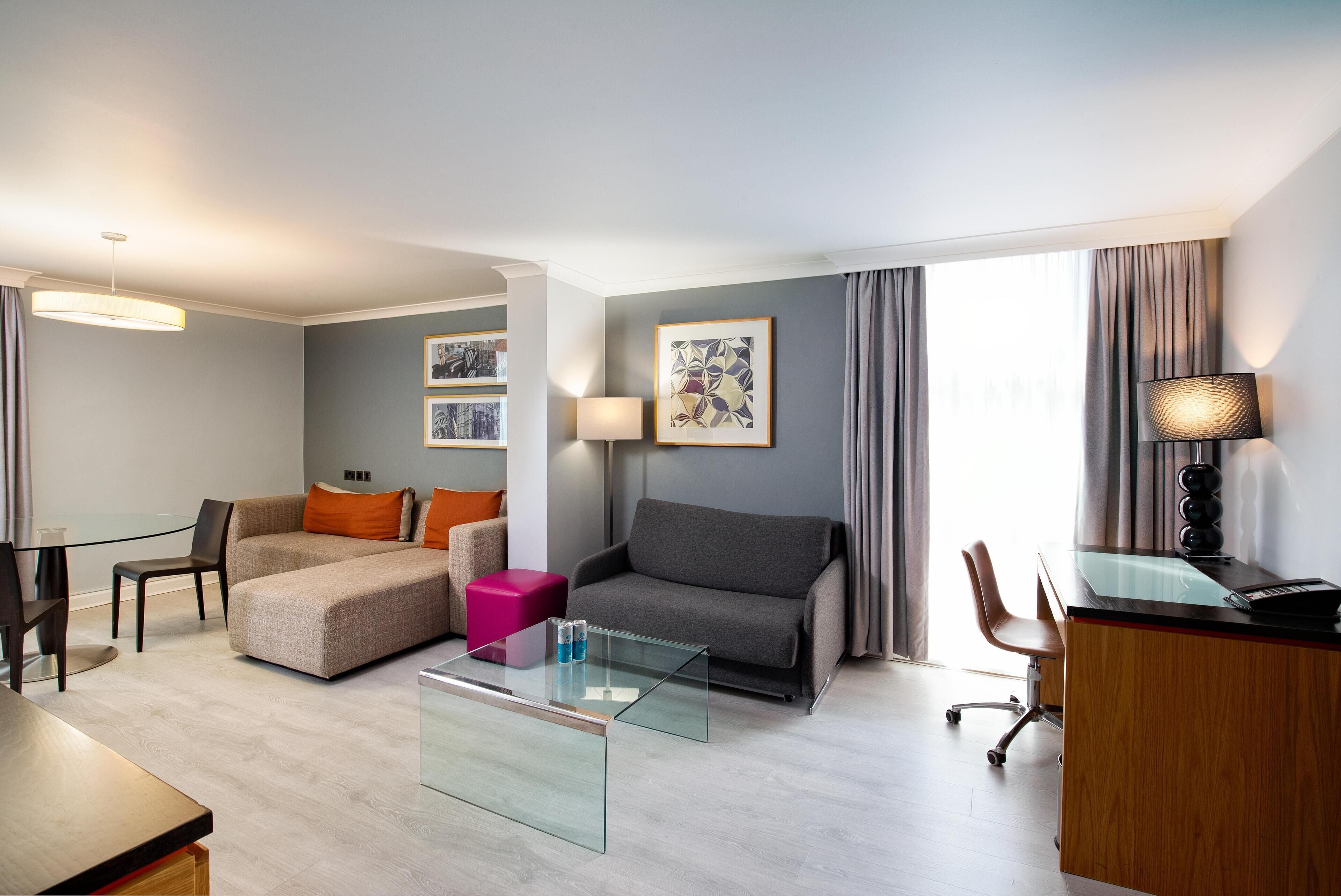 Een moderne hotelkamer met een bank, een glazen salontafel, een bureau en een stoel.