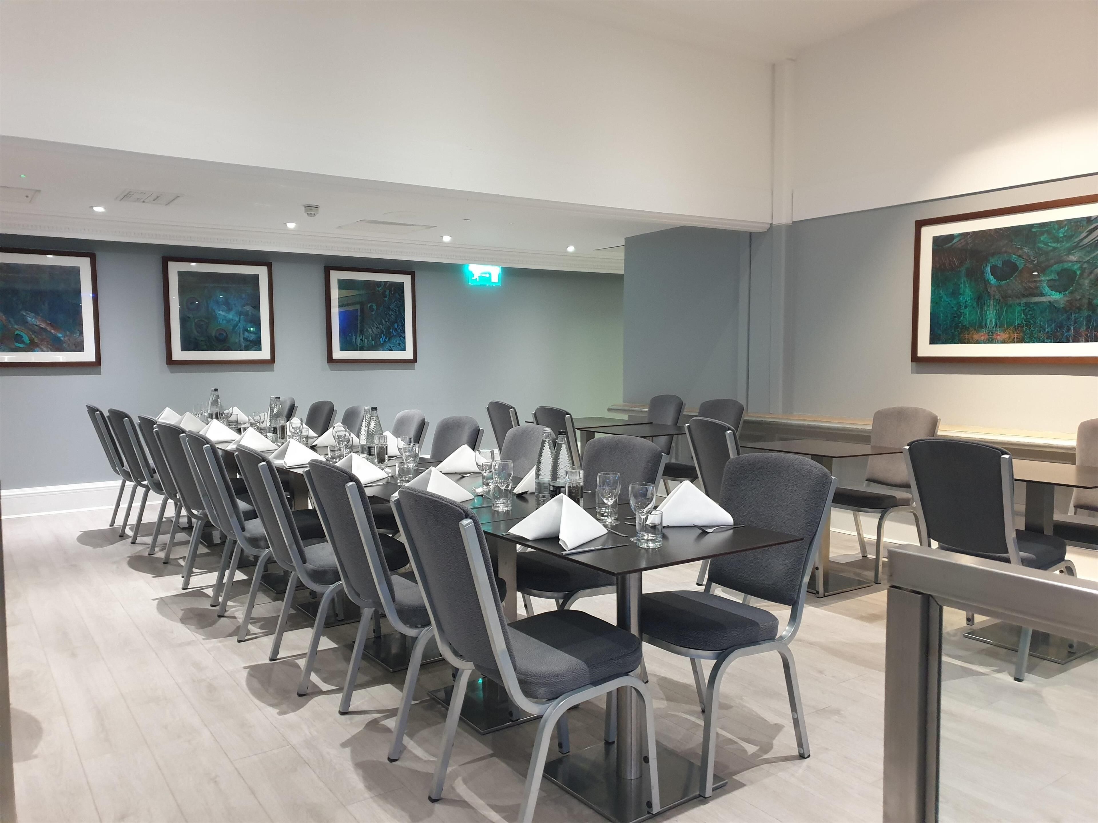 Uma sala de conferências com uma mesa comprida, cadeiras cinzentas e quadros nas paredes.