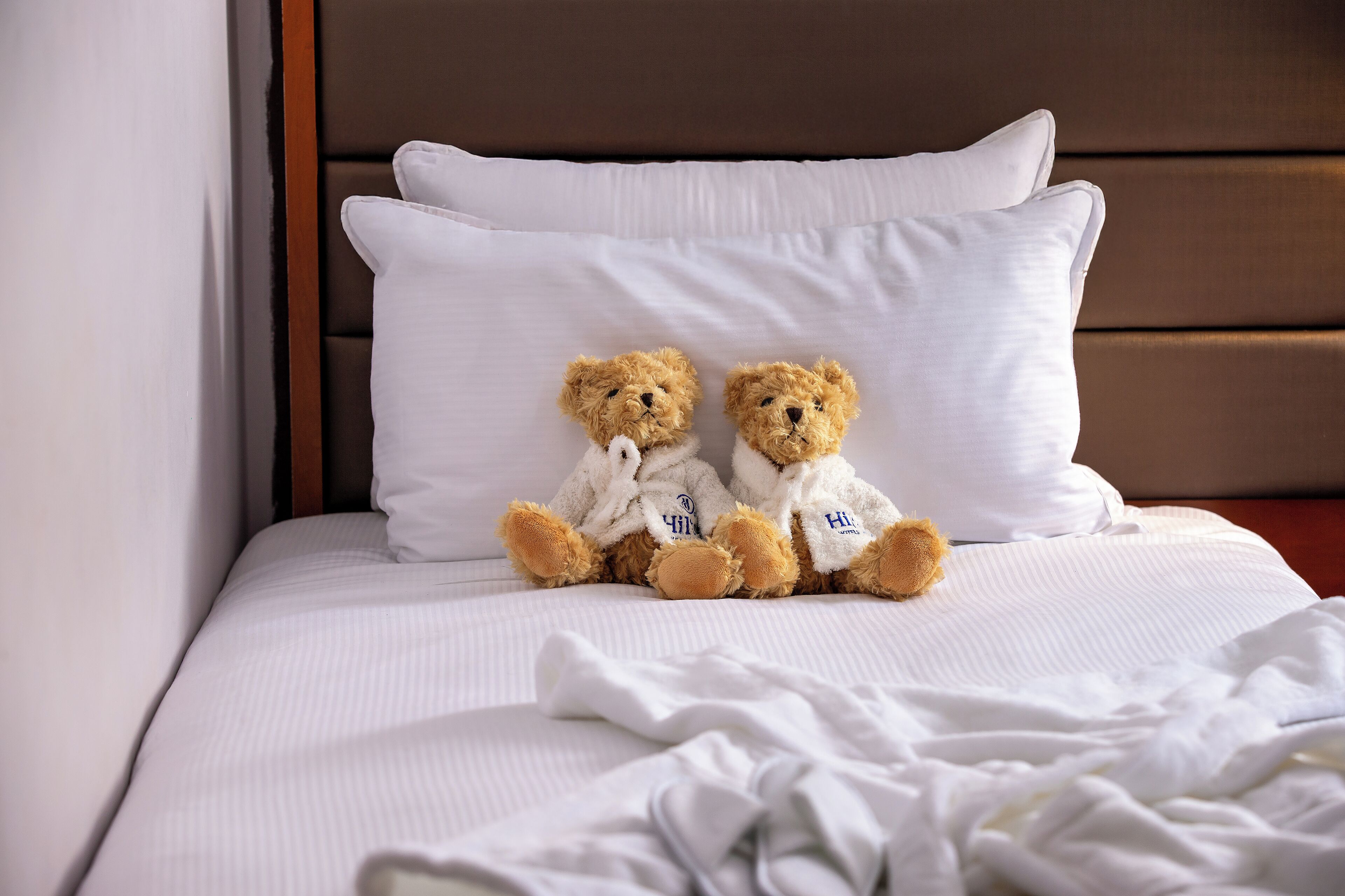 Ein Bett mit weißer Bettwäsche und zwei Teddybären darauf.