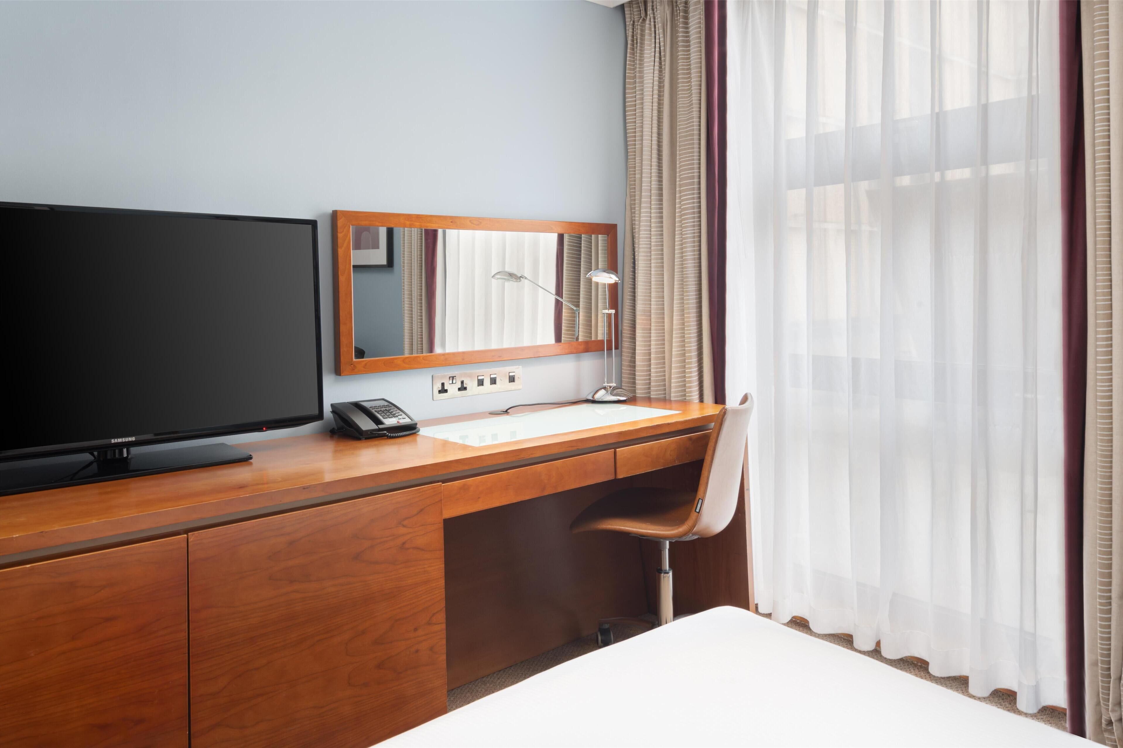 Hotelkamer met een houten bureau, een flatscreen televisie, een telefoon, een spiegel en een stoel.