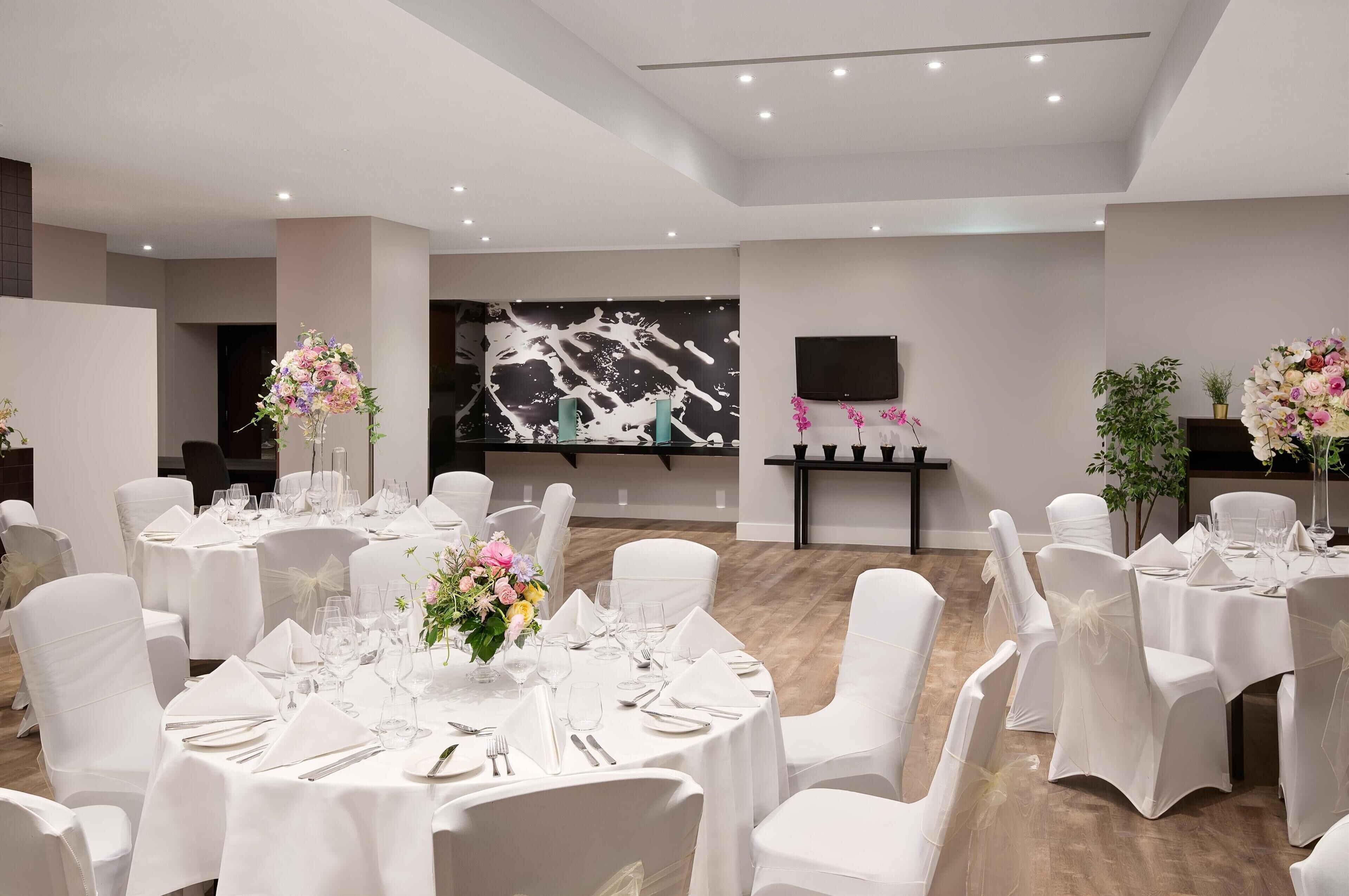 A banquet hall with round tables set for dining, white chairs, and floral centerpieces.