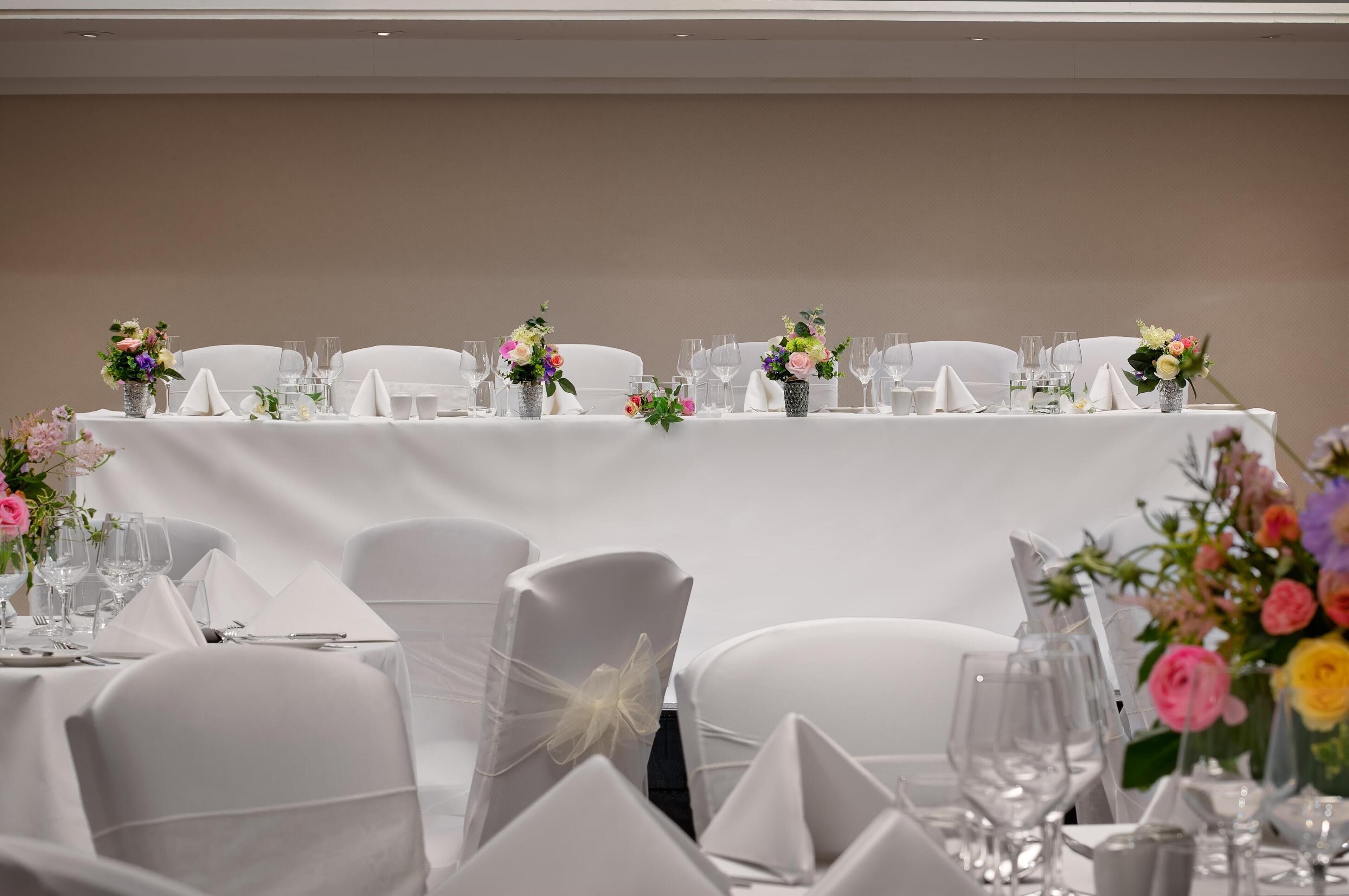 A banquet table with white tablecloths, neatly arranged glassware, and floral centerpieces.
