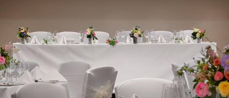 A banquet table with white tablecloths, neatly arranged glassware, and floral centerpieces.