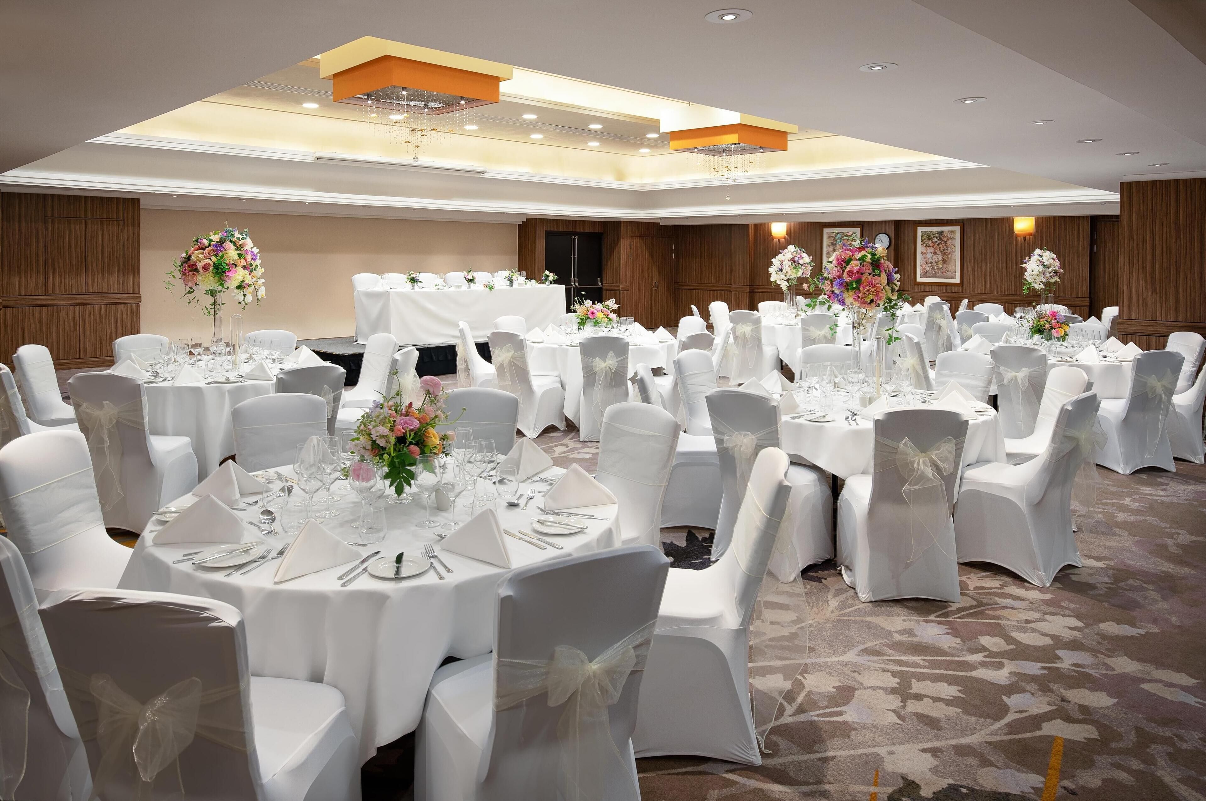 A banquet hall with round tables set for events, white chairs, and floral centerpieces.