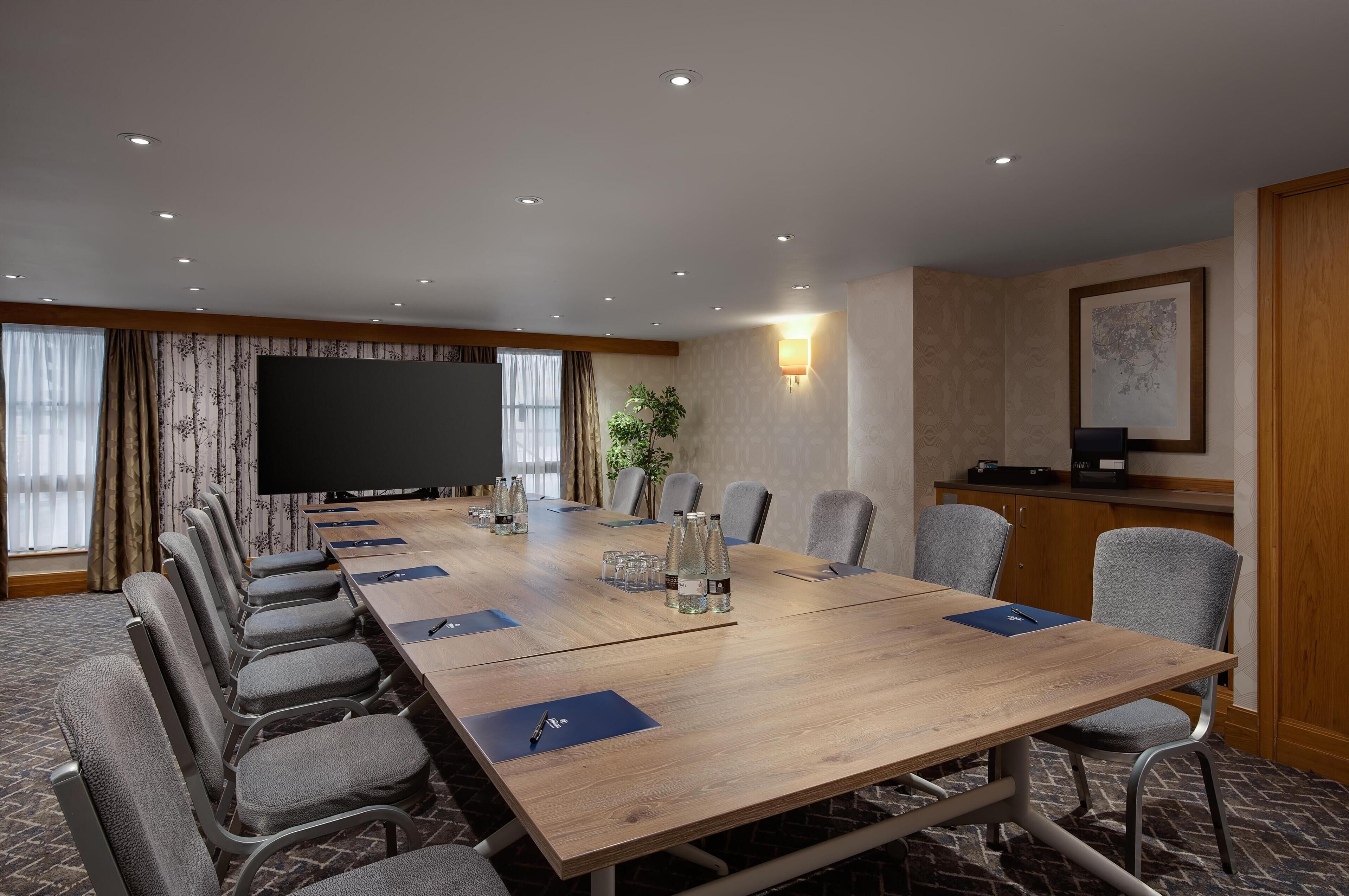 Une salle de conférence avec une longue table, des chaises, un téléviseur et une plante.