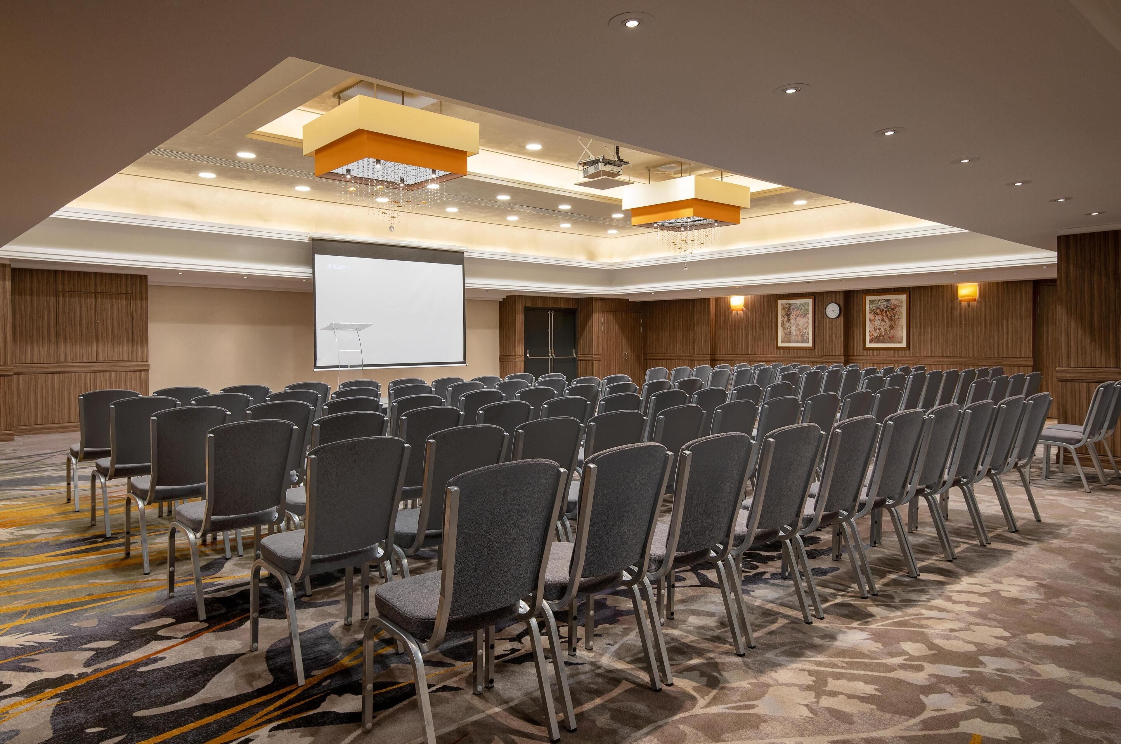 Ein Konferenzraum mit Reihen von Stühlen, einer Projektionsleinwand und einem Teppichboden.
