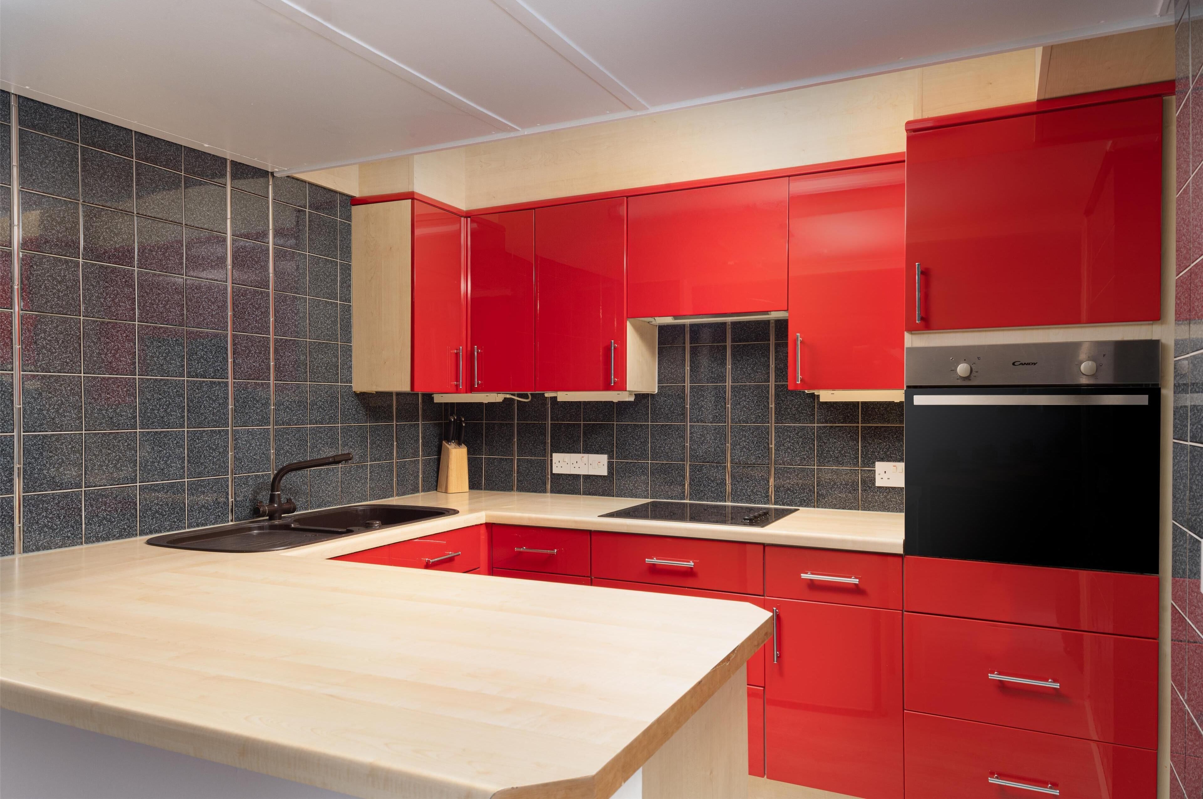 A modern kitchen with red cabinets, a black refrigerator, and a beige countertop.