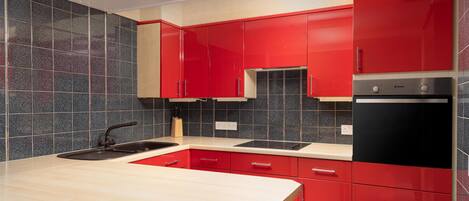 A modern kitchen with red cabinets, a black refrigerator, and a beige countertop.