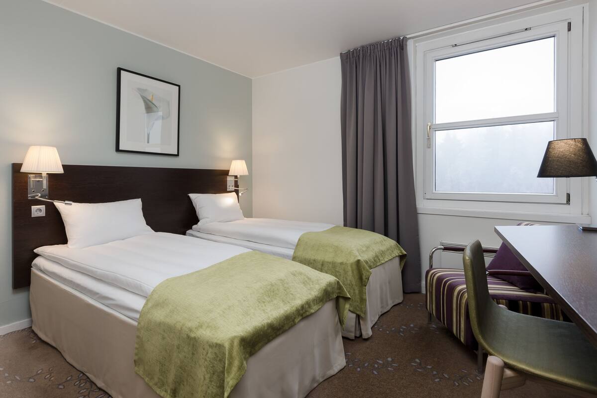 A hotel room with two beds, a desk, a chair, and a window with curtains.
