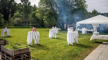 Ett evenemang utomhus med bord täckta av vita dukar, uppställda på en gräsyta med ett tält i bakgrunden.