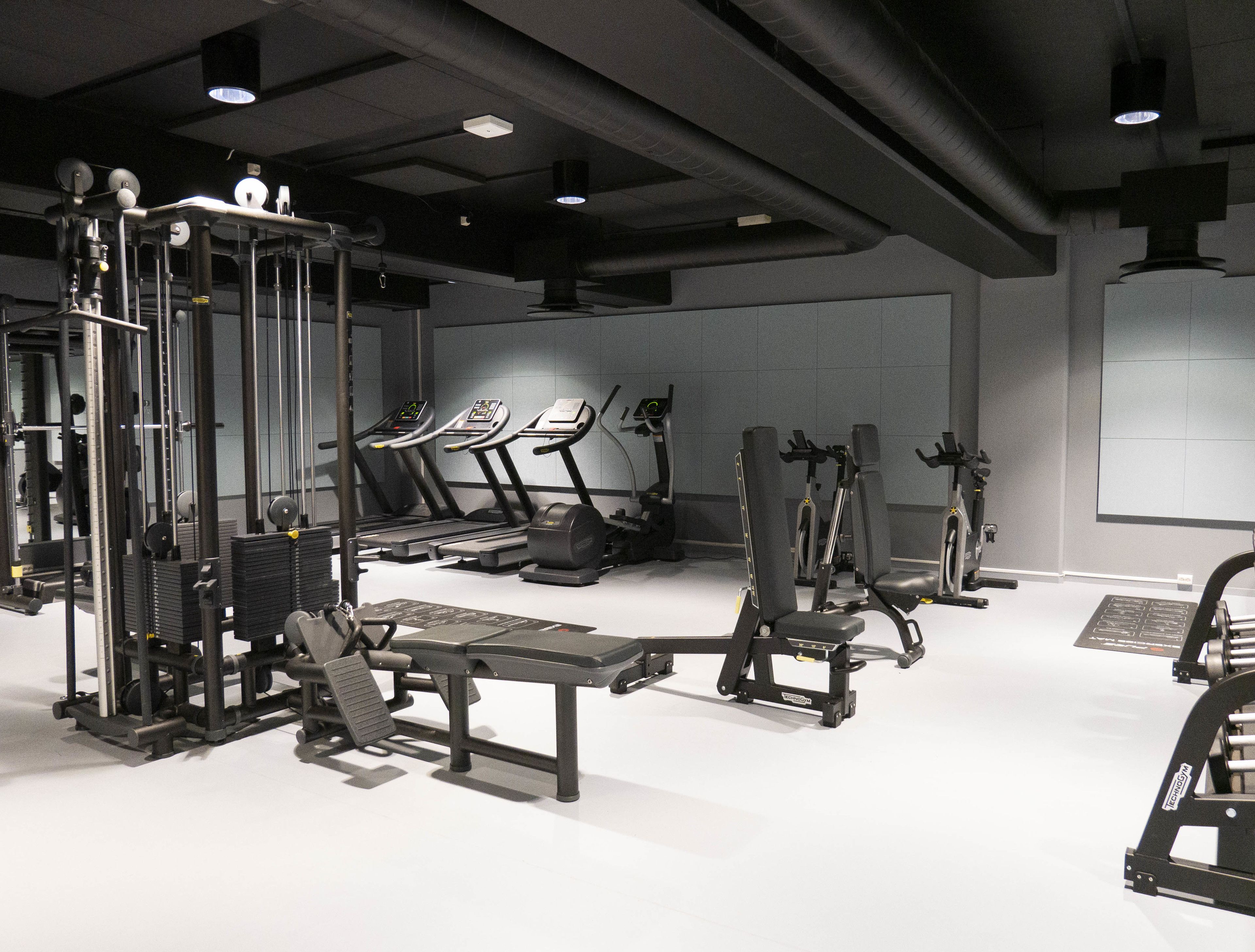 Une salle de sport équipée de divers appareils d’entraînement, notamment des tapis de course, des appareils de musculation et un support à squats.