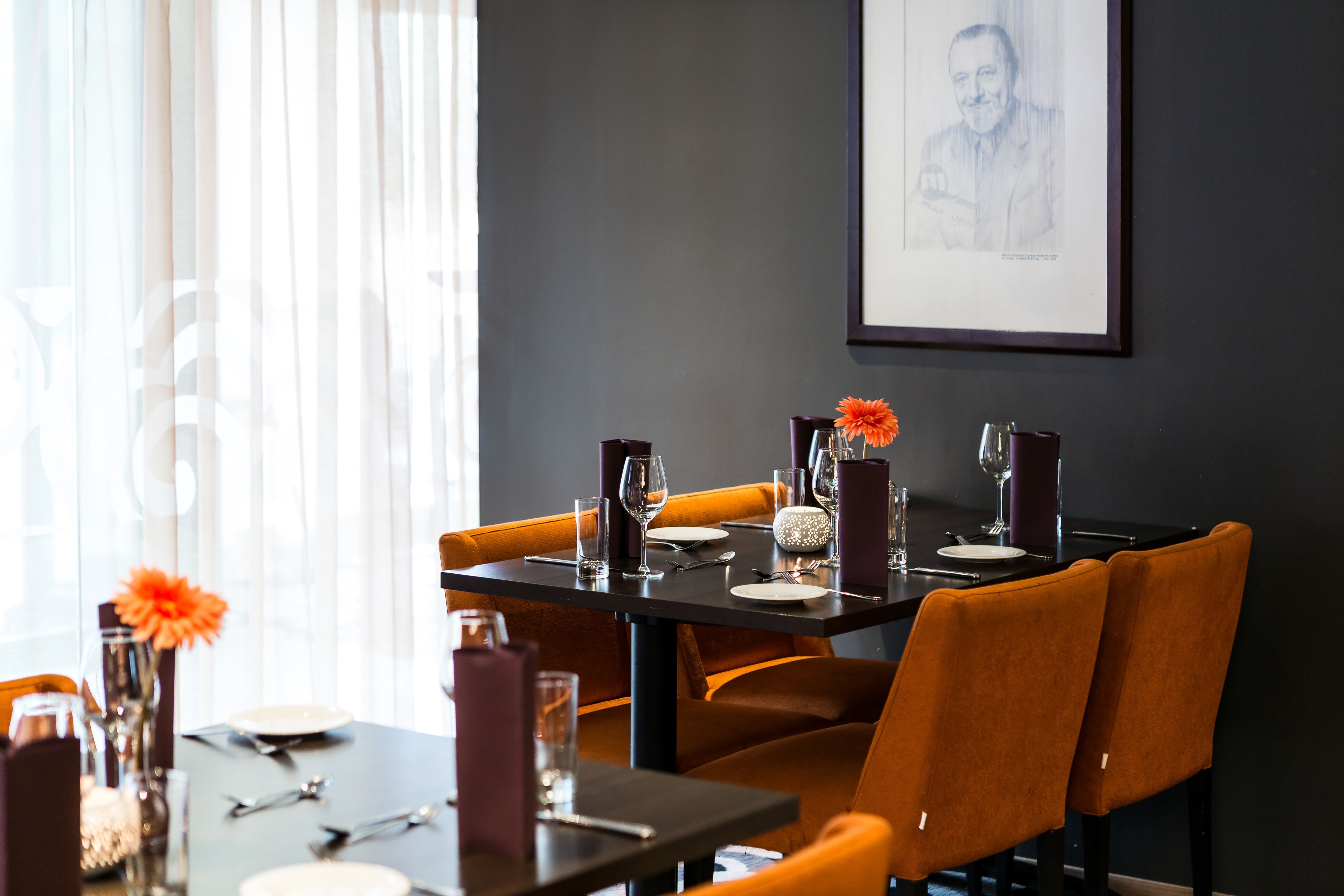 Un comedor con una mesa dispuesta para dos personas, con sillas anaranjadas y una mesa oscura.
