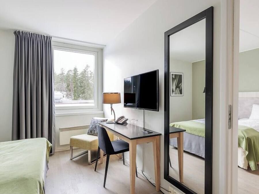 Une chambre d’hôtel avec un lit, un bureau et une chaise, une télévision et un grand miroir.