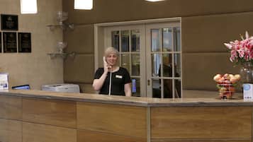 Een receptiebalie met een receptionist, een glazen vitrine en een bloemenvaas.