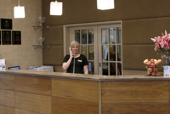A reception desk with a receptionist, a glass display case, and a vase of flowers.