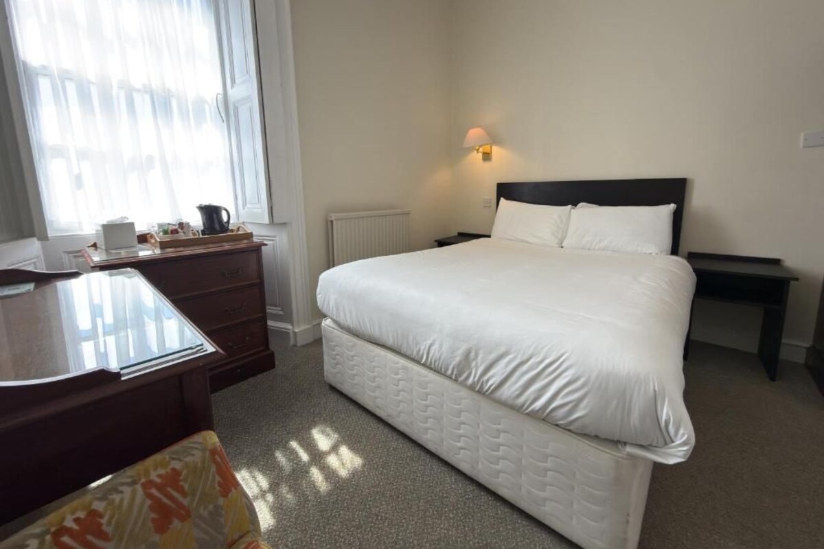 A hotel room with a bed, a desk, a dresser, and a window with curtains.