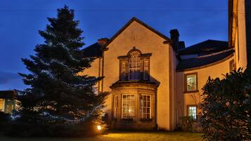 A two-story house with a bay window, a large tree with lights, and a well-maintained lawn.